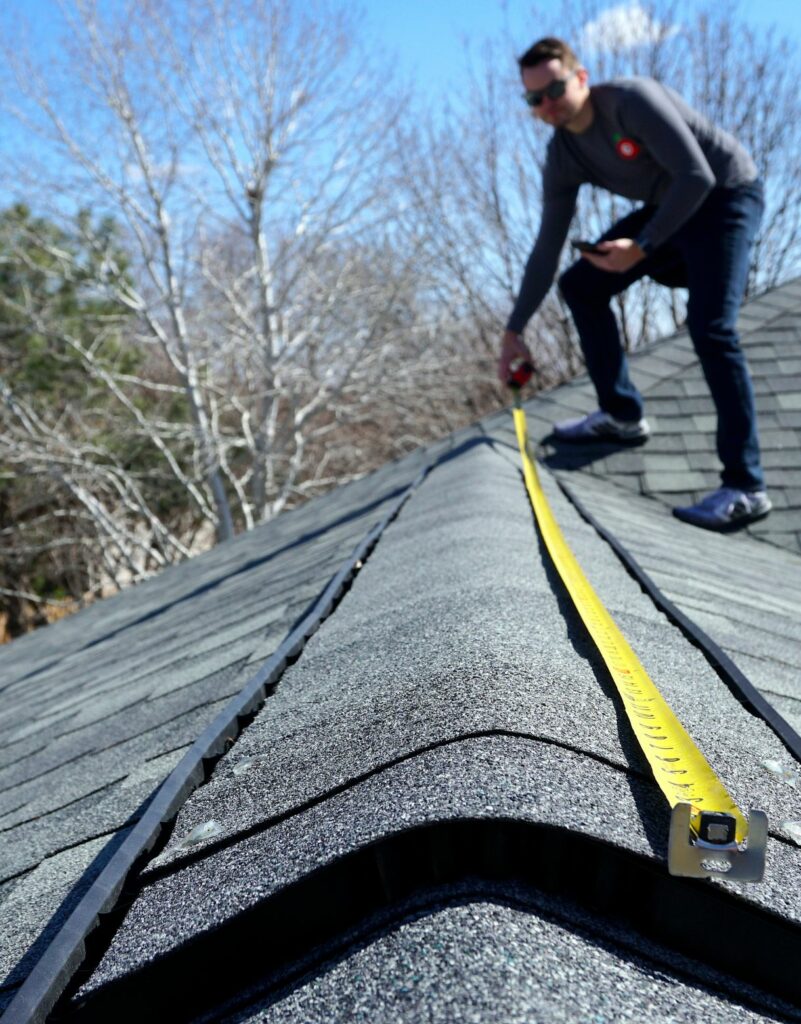 A man on a roof measuring it with a tape measure.
