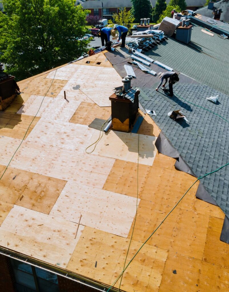 A roof being re-shingled with workers on it.