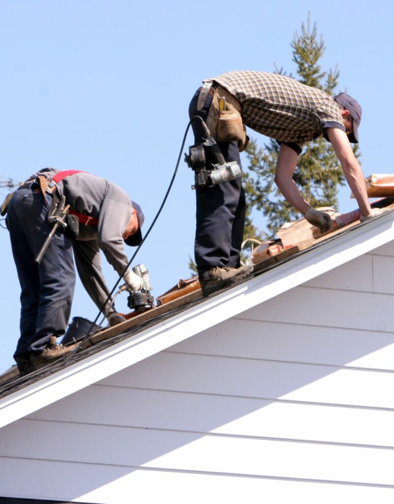 Two men working on a roof with tools.
